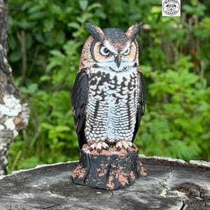 May include: A three-dimensional owl figurine perched on a textured tree stump base. The owl features black, white, and brown plumage with detailed feather patterns and a sharp gaze. A circular logo with the text BIGSHOT TINKERS is visible.