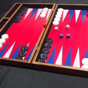 May include: A wooden backgammon game board with a red felt playing surface, black and white playing pieces, and blue and white triangles. The board is open and shows the playing pieces in the middle of the board.