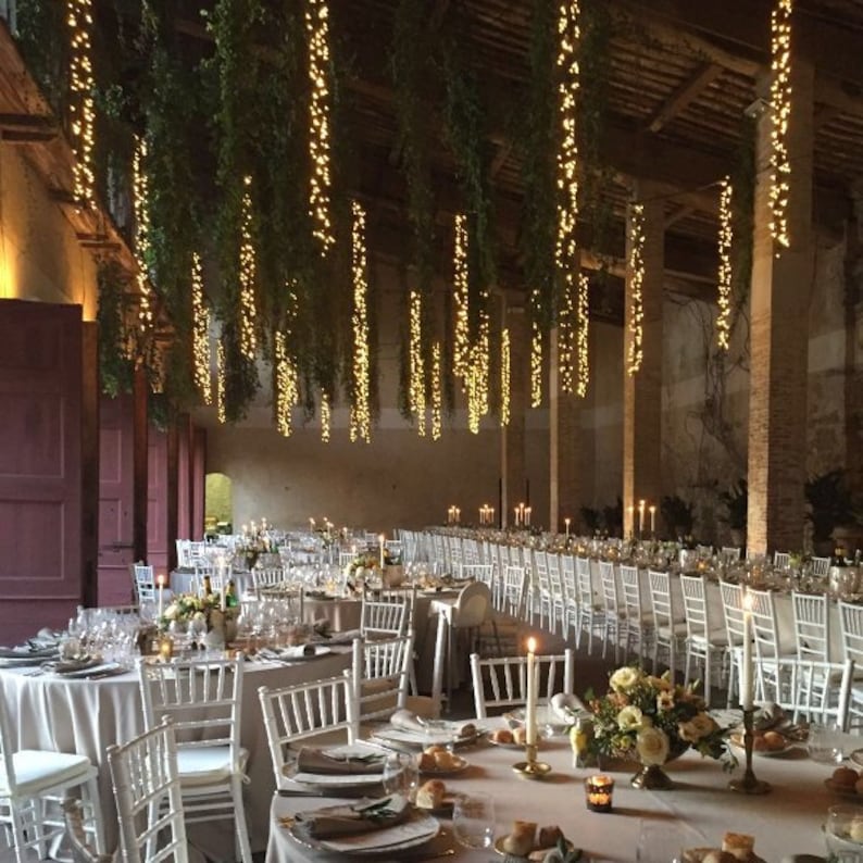 3’ lights hanging with greenery from ceiling over wedding tables