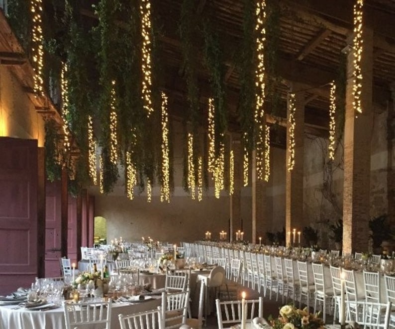 3’ lights hanging with greenery from ceiling over wedding tables