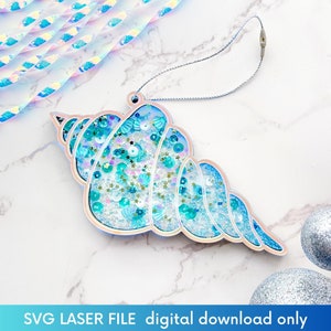 May include: A blue and white seashell ornament with a string for hanging. The seashell is filled with blue and white glitter and sequins.