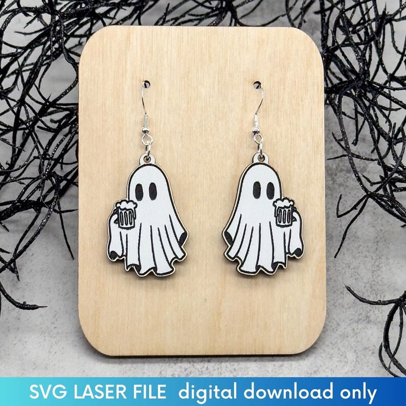 May include: A pair of wooden earrings featuring a ghost holding a beer mug. The earrings are white with black details and are hanging from silver hooks.
