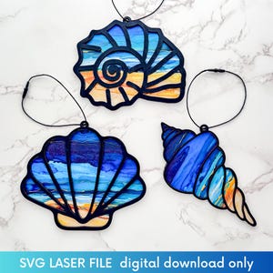 Peut inclure: Trois ornements en forme de coquillage avec des contours noirs et des motifs colorés et abstraits sur le thème de l'océan. Les ornements sont suspendus par des cordons noirs. Le bas de l'image contient le texte "SVG LASER FILE digital download only."