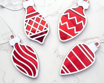May include: Four red and white Christmas ornament SVG laser cut files. The ornaments are in the shape of a teardrop and have different patterns: a grid, zigzags, stripes, and swirls.