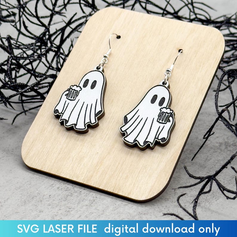 May include: A pair of wooden earrings featuring a ghost holding a beer mug. The earrings are white with black outlines and are hanging from silver hooks.