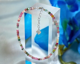 May include: A multi-coloured gemstone bracelet with a silver clasp and a heart charm. The bracelet is displayed on a clear acrylic stand against a white background.