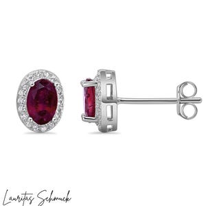 Può includere: Orecchini a lobo in argento con pietre rosse ovali profonde, circondate da piccole pietre trasparenti. Gli orecchini hanno un design classico con chiusura a perno e farfalla. Il nome del marchio "Lauritas Schmuck" è scritto in corsivo in basso.