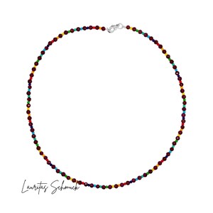 Puede incluir: Un collar de cuentas de colores con un cierre plateado. El collar presenta pequeñas cuentas redondas en tonos rojo, amarillo, verde, azul y morado. El collar se muestra sobre un fondo blanco.