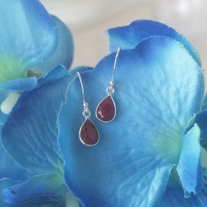 Könnte beinhalten: Ein Paar silberne Ohrhänger mit tropfenförmigen roten Edelsteinen.