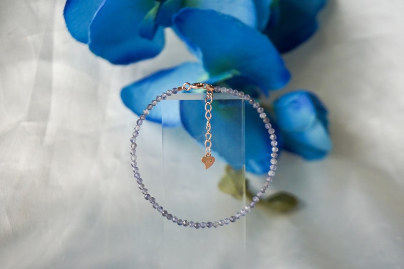 May include: A delicate bracelet made of small, light purple beads with a rose gold chain and heart charm.