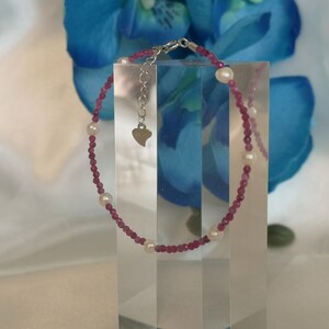 May include: A pink and white beaded bracelet with a heart charm. The bracelet is made with small pink beads and larger white beads.