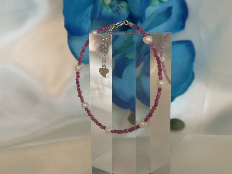 May include: A pink and white beaded bracelet with a heart charm. The bracelet is made with small pink beads and larger white beads.