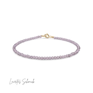 Könnte beinhalten: Ein zartes Armband aus violetten Kristallperlen mit einem goldenen Verschluss. Das Armband besteht aus kleinen, runden Perlen und hat ein schlichtes, elegantes Design.