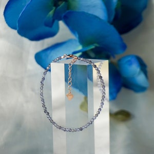 May include: A delicate bracelet made of small, light purple beads with a rose gold clasp and a heart charm.