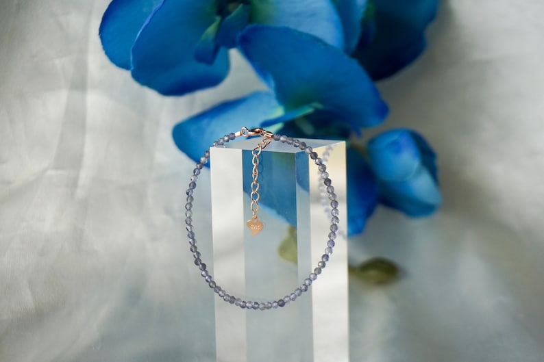 May include: A delicate bracelet made of small, light purple beads with a rose gold clasp and a heart charm.