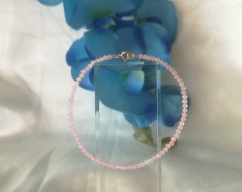 May include: A delicate pink gemstone bracelet with a silver clasp. The bracelet is made of small, round beads and is displayed on a clear stand.