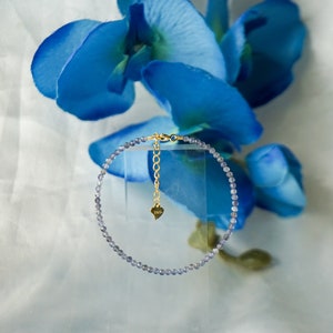 May include: A delicate bracelet made of small, light blue beads with a gold chain and heart charm.