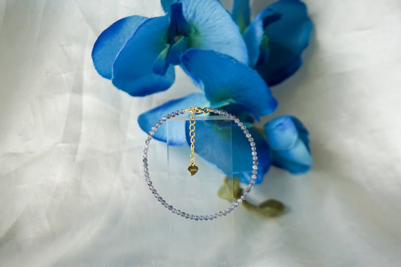 May include: A delicate bracelet made of small, light blue beads with a gold chain and heart charm.