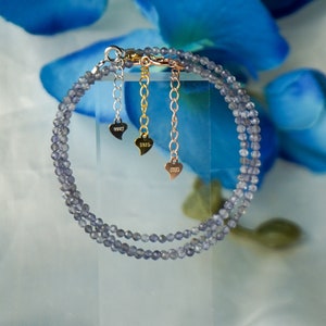 May include: A double strand bracelet made of small, light blue, faceted beads. The bracelet has a silver clasp and three gold heart charms with the year 2023 engraved on each.
