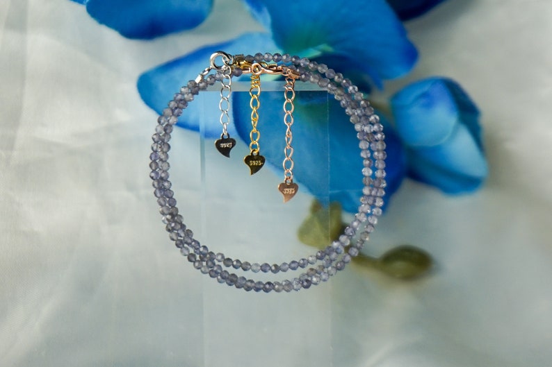 May include: A double strand bracelet made of small, light blue, faceted beads. The bracelet has a silver clasp and three gold heart charms with the year 2023 engraved on each.