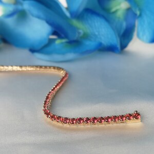 May include: A gold tennis bracelet with a row of small, round, red gemstones.