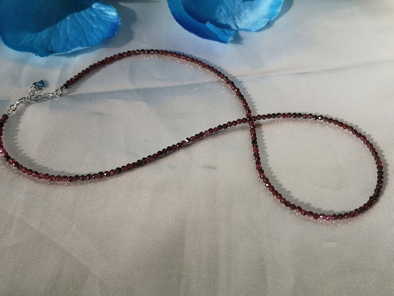 May include: A delicate necklace made of small, dark red garnet beads. The necklace is strung on a silver chain and has a small heart-shaped charm.