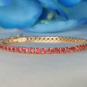 May include: A gold bracelet with a row of pink gemstones. The bracelet is made of a thin metal band with a clasp.