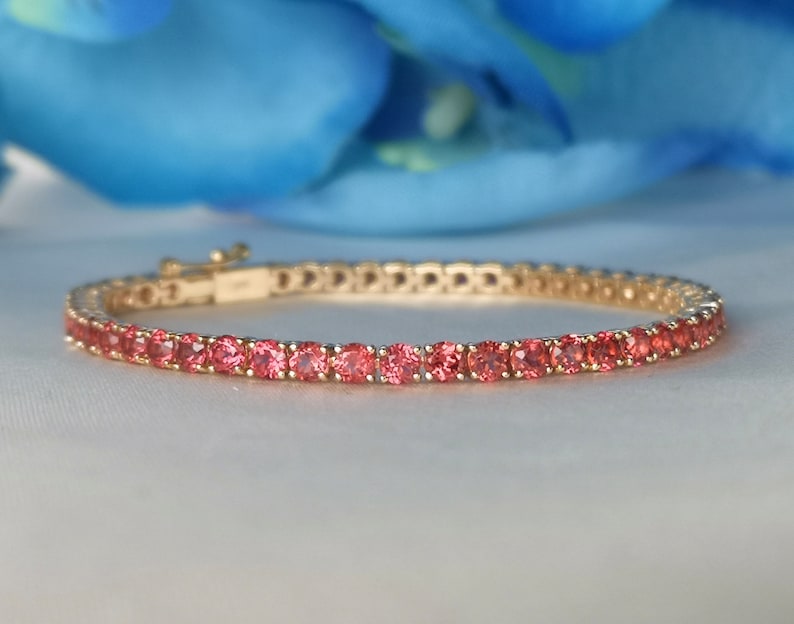 May include: A gold bracelet with a row of pink gemstones. The bracelet is made of a thin metal band with a clasp.