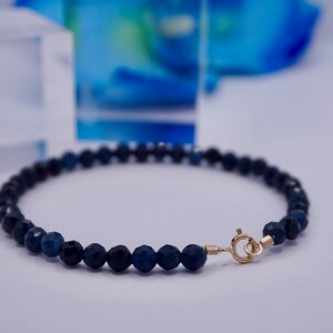 May include: A dark blue gemstone bracelet with a gold clasp. The bracelet is made of faceted beads and is approximately 7 inches in length.