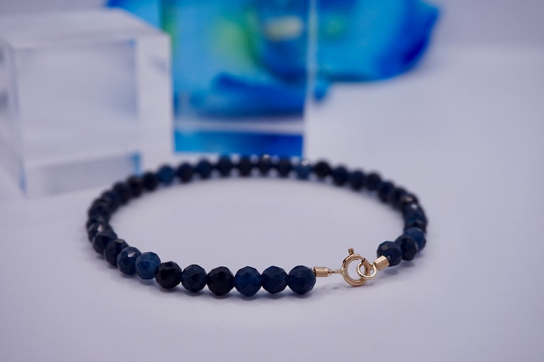 May include: A dark blue gemstone bracelet with a gold clasp. The bracelet is made of faceted beads and is approximately 7 inches in length.