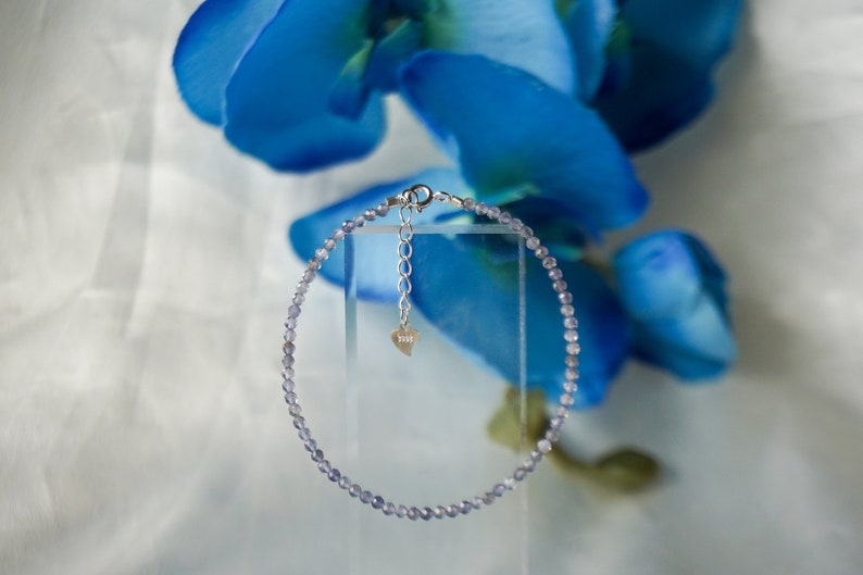 May include: A delicate silver chain bracelet with a heart charm and small, light purple beads.