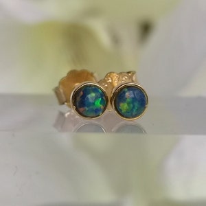 Puede incluir: Un par de pendientes de botón de oro con piedras redondas de ópalo iridiscente. Los ópalos tienen un color azul, verde y amarillo.