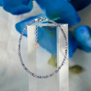 May include: A delicate silver bracelet with a heart charm, featuring a strand of small, light purple beads.