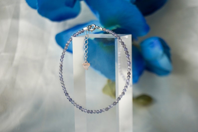 May include: A delicate silver bracelet with a heart charm, featuring a strand of small, light purple beads.