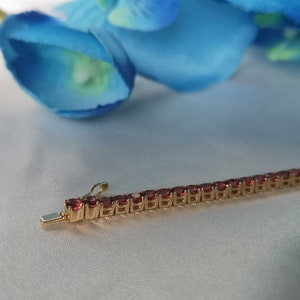 May include: A gold chain bracelet with small, red gemstones. The bracelet is on a white surface.
