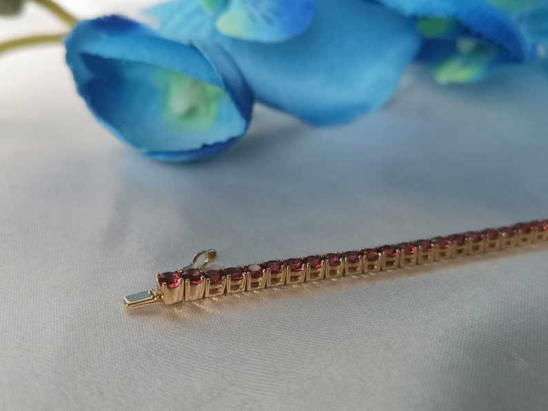 May include: A gold chain bracelet with small, red gemstones. The bracelet is on a white surface.