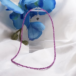 Puede incluir: Un delicado collar de piedras preciosas rosas con un cierre plateado y un pequeño dije en forma de corazón. El collar está hecho de pequeñas cuentas redondas y mide aproximadamente 45 cm de largo.