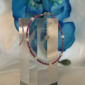 May include: A delicate bracelet with pink and white beads. The bracelet has a silver heart charm and a silver clasp.