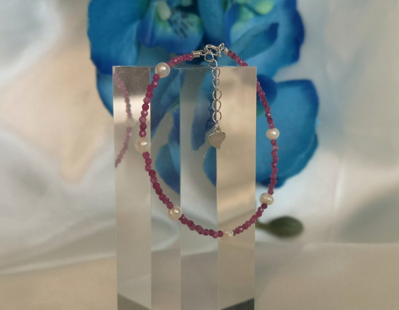 May include: A delicate bracelet with pink and white beads. The bracelet has a silver heart charm and a silver clasp.