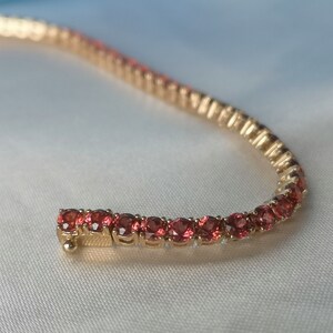 May include: A gold bracelet with a row of small, round, red gemstones.