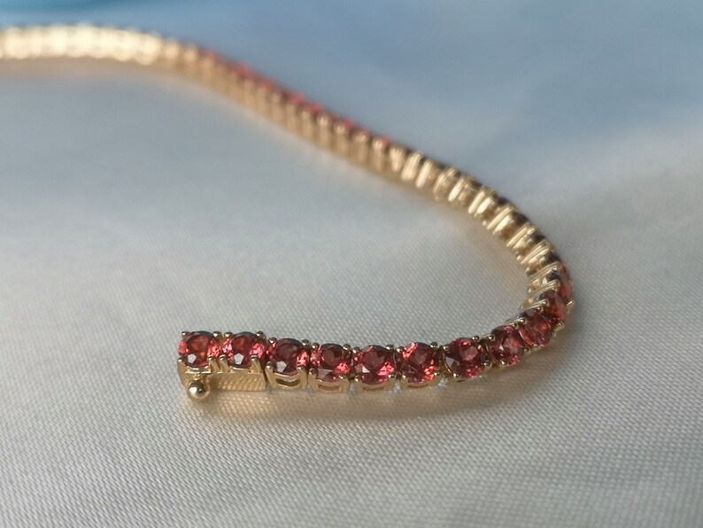 May include: A gold bracelet with a row of small, round, red gemstones.