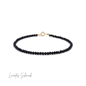 Op de afbeelding: Fijn zwart kralenarmbandje met een goudkleurige sluiting. De armband heeft kleine, ronde, zwarte kralen. De sluiting is eenvoudig van ontwerp. Het woord "Lauritas Schmuck" staat onderaan in cursief.
