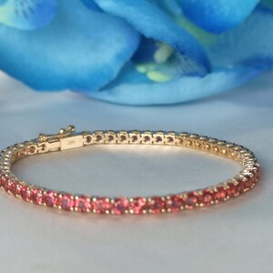 May include: A gold tennis bracelet with pink gemstones. The bracelet is made of a delicate chain with small, round stones.