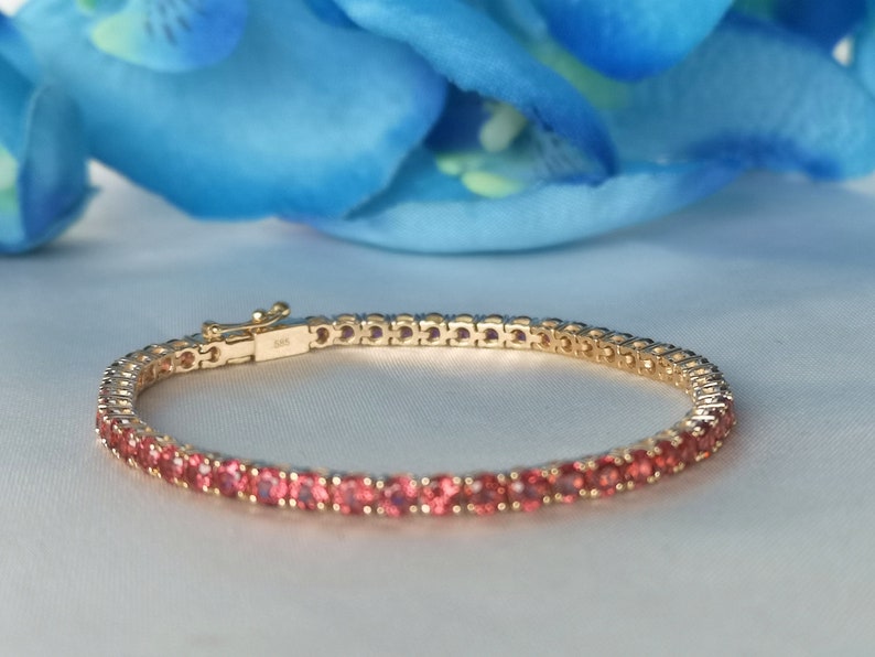 May include: A gold tennis bracelet with pink gemstones. The bracelet is made of a delicate chain with small, round stones.