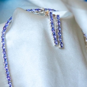 Op de afbeelding: Een zilveren ketting en oorbellen set met een rij ovale paarse edelstenen.