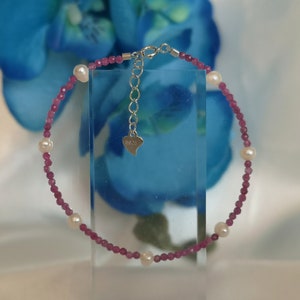 May include: A pink and white beaded bracelet with a silver clasp. The bracelet has a heart-shaped charm with the word "925" on it.