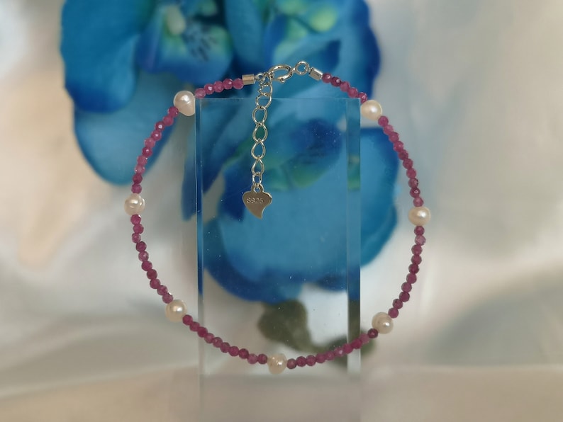 May include: A pink and white beaded bracelet with a silver clasp. The bracelet has a heart-shaped charm with the word "925" on it.