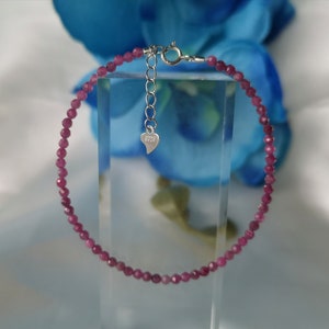 Op de afbeelding: Een delicate armband van roze edelstenen met een zilveren sluiting en een hartvormige hanger met de tekst "925".