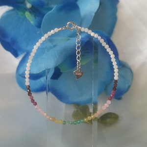May include: A rainbow gemstone bracelet with a silver clasp and a heart-shaped tag that says "925".