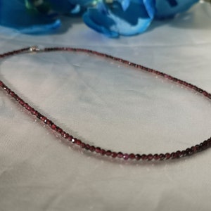 May include: A delicate necklace made of small, dark red garnet beads. The necklace is strung on a silver chain and is approximately 18 inches long.